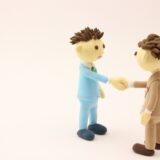 スーツ姿の人物が握手しているクレイ風イメージ画像