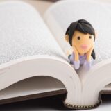遺言の書き直しや訂正方法を確認する人をイメージした、開いた本と人形の写真