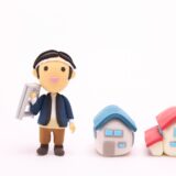 相続した実家を前に立つ男性と2軒の家の模型